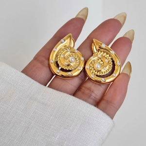 Golden spiral seashell stud earrings with white pearl accents shown on hand model