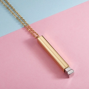 Close-up of golden vertical bar pendant with silver cube detail on two-tone background