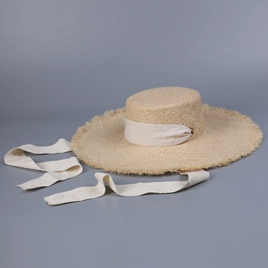 Detail of wide brim straw hat featuring frayed edges and cream ribbon through metal rings