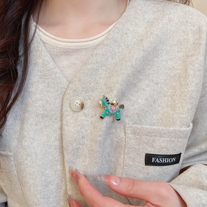 Detail of teal enamel horse brooch with gold ingot on a beige cashmere sweater