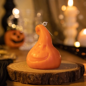 Detail of orange pumpkin candle with ghost face on rustic wooden base for Halloween decor