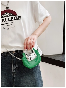 Detail of green mini crossbody bag with silver metal handle and glossy finish on a model