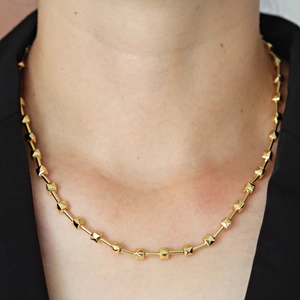 Dettaglio di una collana a catena in bambù bicolore con accenti dorati su una modella
