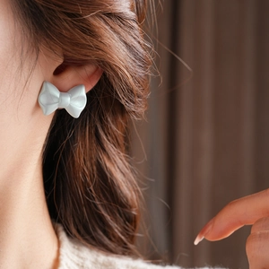 Close-up of matte blue bow-knot stud earring worn on ear with soft resin texture