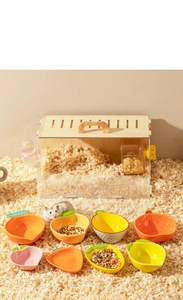 Detailed view of various fruit-shaped ceramic hamster bowls in a natural cage setting