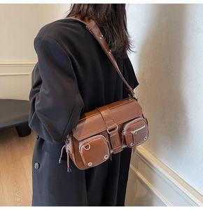 Close-up of brown leather bag with silver zippers and D-rings on a model in dark coat