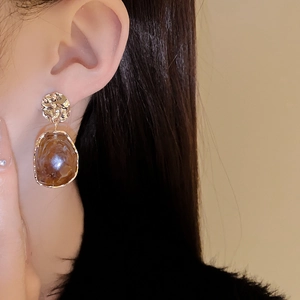 Close-up of irregular round earrings with brown translucent pendant on model's ear