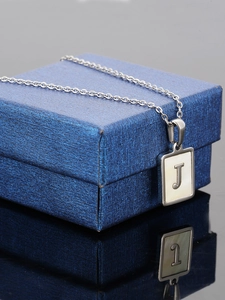Macro shot of silver letter J pendant with white shell inlay on a blue jewelry box