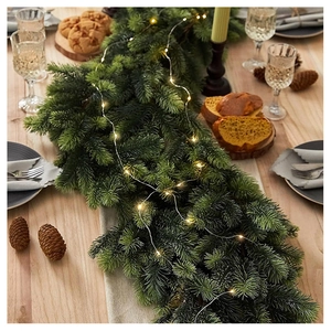 Lush evergreen pine garland with warm LED lights arranged on a wooden dining table