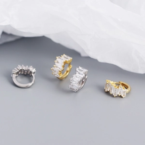 Close-up of gold and silver S925 earrings with rectangular zircons on paper background
