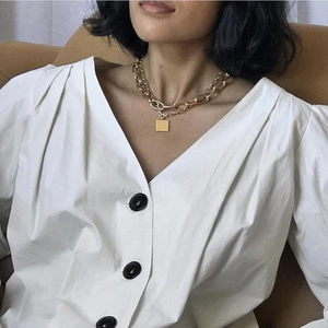 Close-up of gold chunky chain necklace with square pendant on female model
