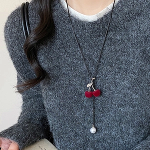 Detailed view of red flocked cherry pendant with pearl on a black woven sweater chain