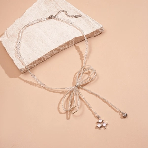 Bow heart pendant necklace with glass beads on natural stone display, minimalist silver style