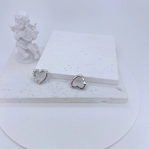 Detailed view of silver heart earrings with zircon inlay on a white textured surface