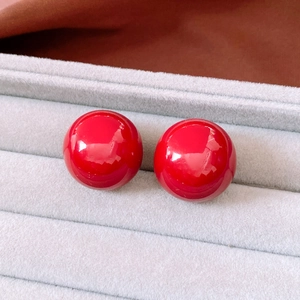Close-up of bright red spherical stud earrings with glossy finish in a grey jewelry tray