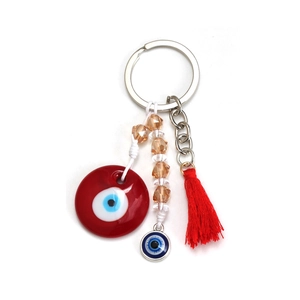 Macro detail of the red Evil Eye keychain featuring amber beads and a silky tassel pendant