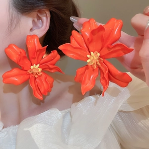 Close-up of oversized orange acrylic flower earrings worn by a model in a resort style