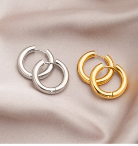 Flat lay of gold and silver thick hoop earrings on soft pink silk fabric texture