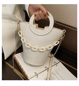 Detail of cream bucket bag featuring resin link chain and gold metal shoulder strap