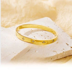 Detailed macro view of gold clover bangle with inlaid diamonds on stone surface