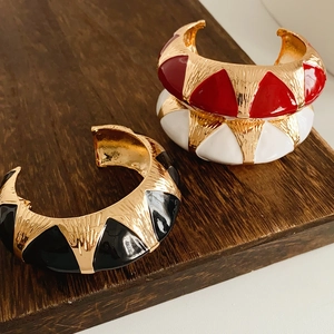 Macro detail of vintage enamel cuff bracelets in red, black, and white gold finishes