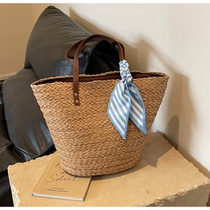 Close-up of woven straw tote bag featuring brown handles and blue striped scarf on stone