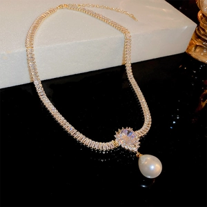 Detailed close-up of gold plated necklace with zircon stones and a teardrop pearl pendant
