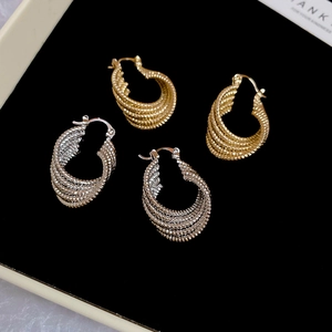 Macro detail of twisted multi-layer hoop earrings in polished gold and silver metal finishes