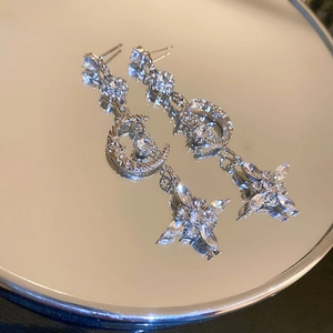 Detailed view of silver star and moon tassel earrings reflecting on a mirror surface