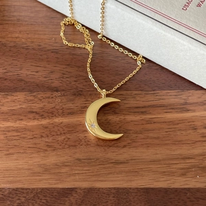 Detail of gold moon pendant with sparkling cubic zirconia on a rustic wooden texture