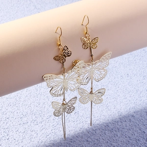Detailed close-up of long gold hollow butterfly earrings on a neutral beige display