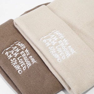 Close-up of high-quality knitted beanies featuring white motivational embroidery details