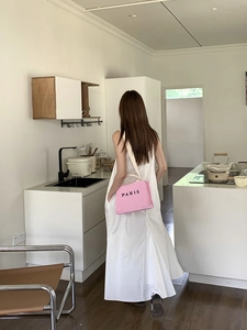 Pink woven straw tote bag with black Paris lettering worn by a model in a white dress