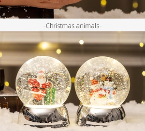 Close-up of glass Christmas snow globes with Santa and snowmen on white snowy surface