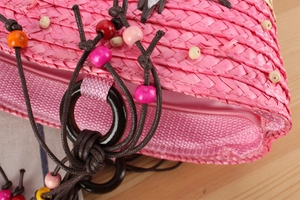 Détail de pochette en paille rose avec perles en bois et fermeture éclair de qualité