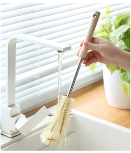 Vue détaillée de la brosse à bouteilles à manche en bois rincée sous l'eau dans la cuisine