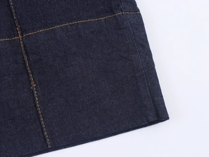 Dettaglio macro del tessuto denim blu scuro con doppie cuciture arancioni a contrasto