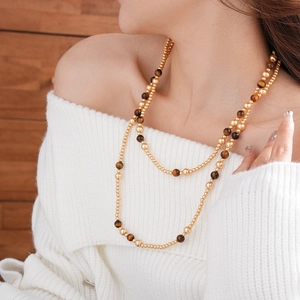 Double-layered beaded necklace with tiger eye texture and gold beads on white knitwear