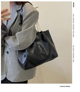 Détail du sac cabas en cuir noir avec chaîne dorée sur une veste de blazer grise