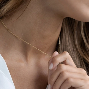Detailed shot of a delicate gold satellite chain necklace worn on a woman's collarbone