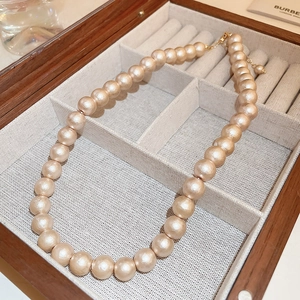 Dettaglio di perle oro champagne opache con chiusura dorata su portagioie in legno scuro