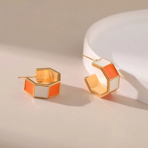 Detailed view of C-shaped hexagon earrings with orange and white enamel on gold metal