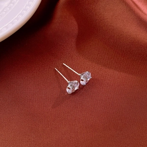 Macro shot of silver zircon stud earrings with classic four-prong setting on silk fabric