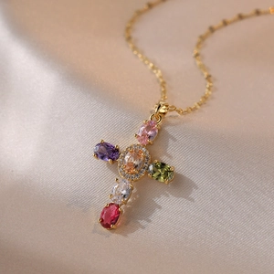 Cross necklace with colorful zircon stones on gold chain over satin fabric background