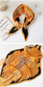 Detail of pleated silk scarf with orange floral pattern displayed on a white surface