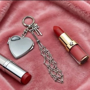 Silver heart mirror bag charm with bow and metal fringe on pink plush surface