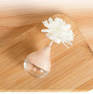Modern glass reed diffuser bottle with a white sola flower on a wooden tray