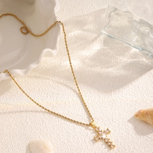 Detail view of a gold cross pendant necklace with sparkling zircons on a seashell