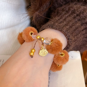 Détail d'un bracelet en boules de peluche marron avec pendentif fleur dorée et perles