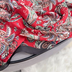Macro detail of red paisley silk scarf showing smooth texture and fine black hem edges
